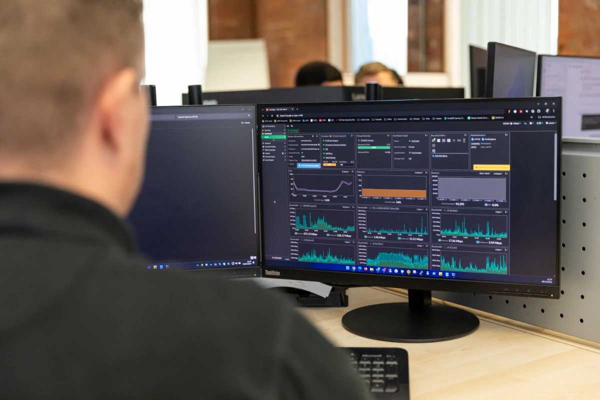 IT professional monitoring system performance metrics on dual computer screens