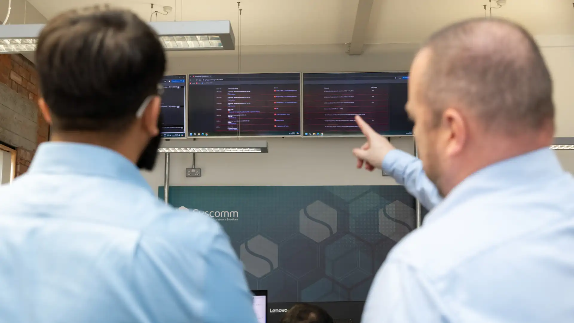 Two IT professionals in light blue shirts analyzing network activity on multiple large screens