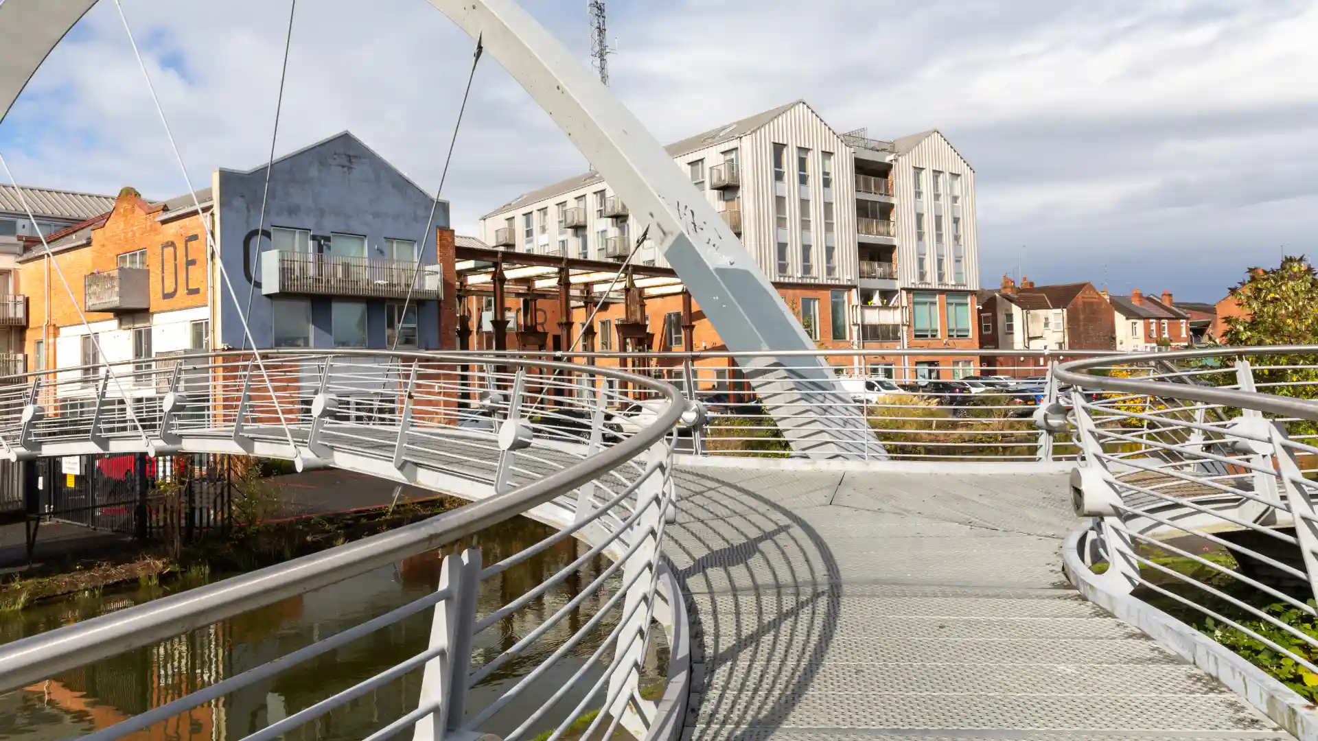 A curved pedestrian bridge with metal railings leading towards a modern residential and office area.webp